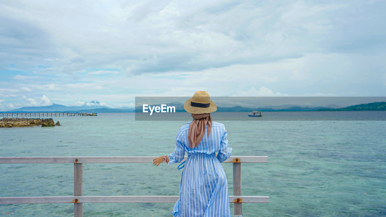 water, vacation, sea, sky, one person, ocean, nature, cloud, blue, hat, adult, clothing, beauty in nature, shore, women, scenics - nature, coast, travel, land, holiday, trip, day, standing, tranquility, leisure activity, transportation, tranquil scene, nautical vessel, beach, travel destinations, sun hat, outdoors, lifestyles, tourism, three quarter length, bay, rear view, horizon, summer, railing, casual clothing, female, young adult, idyllic, looking, relaxation, fashion, person, full length, straw hat