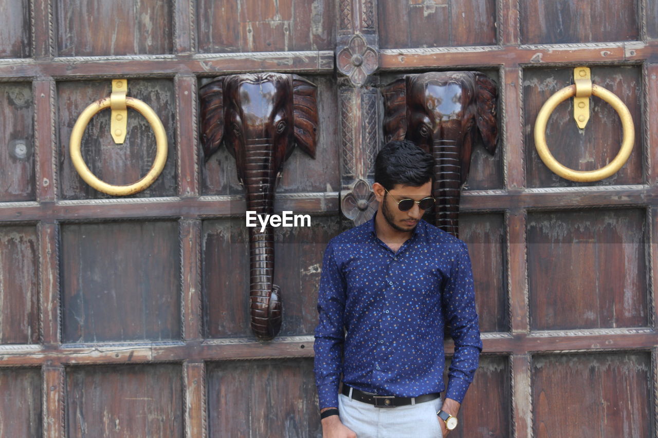 Man wearing sunglasses standing by wooden door