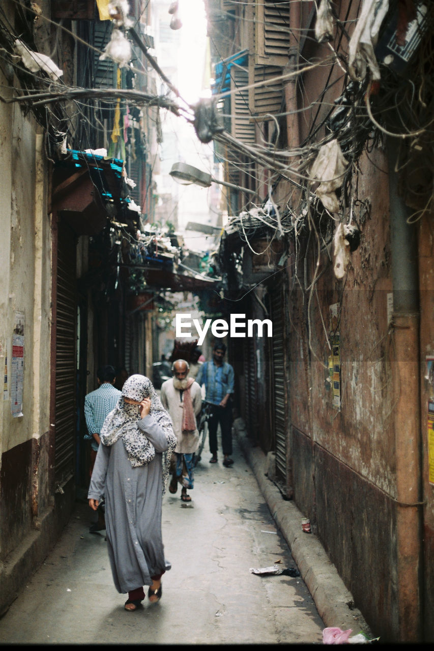 PEOPLE WALKING IN ALLEY AMIDST BUILDINGS