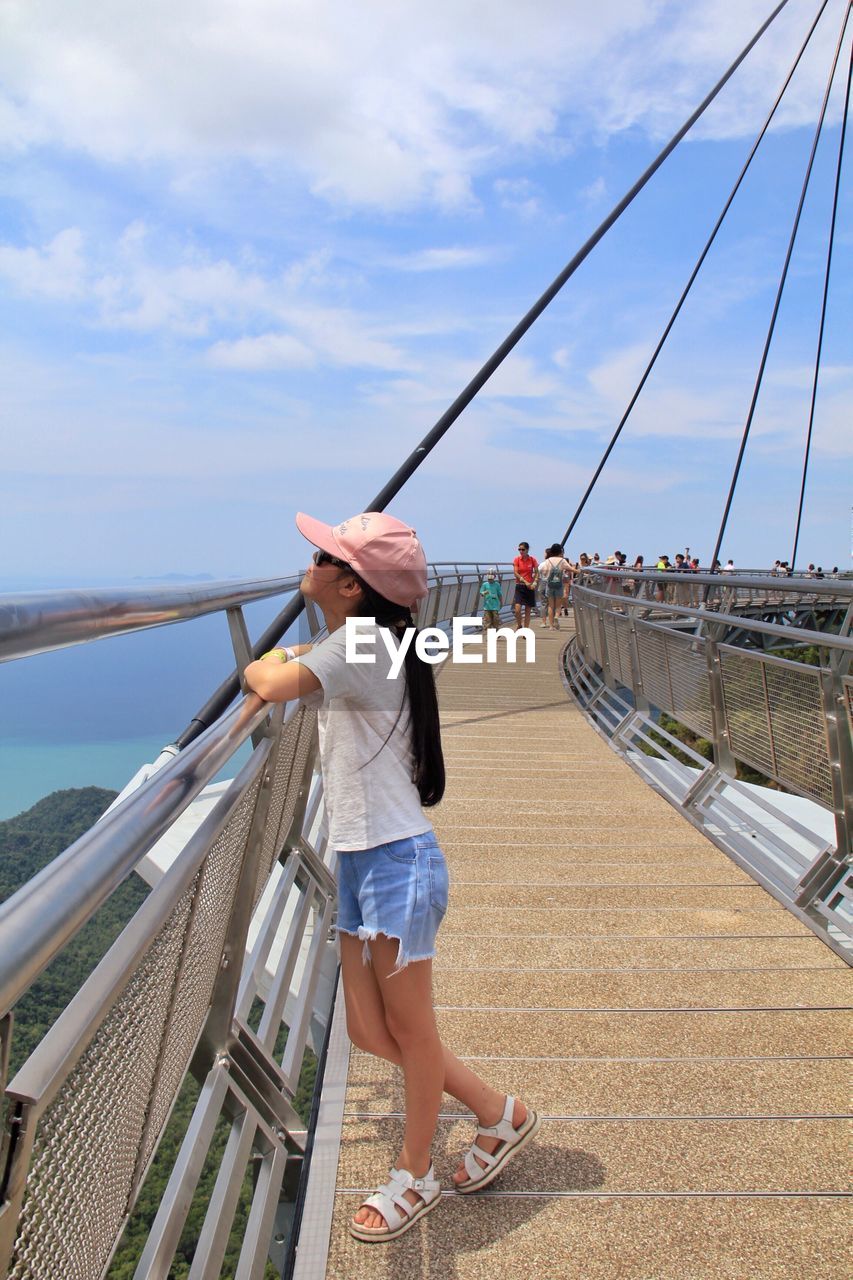 Side view of girl standing on footbridge against sky