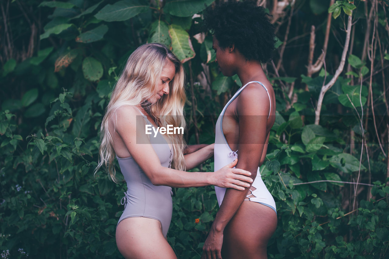 Side view of women standing face to face against plants