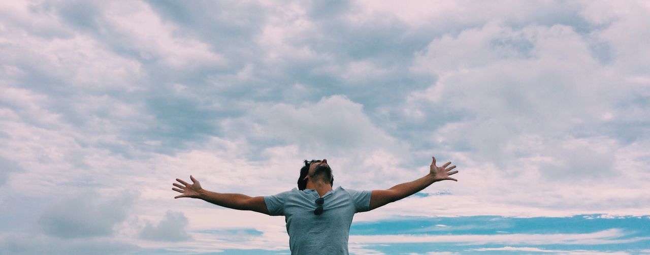 Man with arms outstretched against cloudy sky