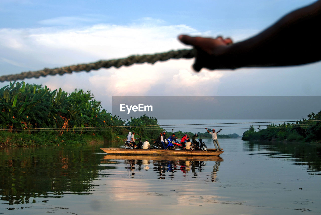 People sitting in boat over lake against sky