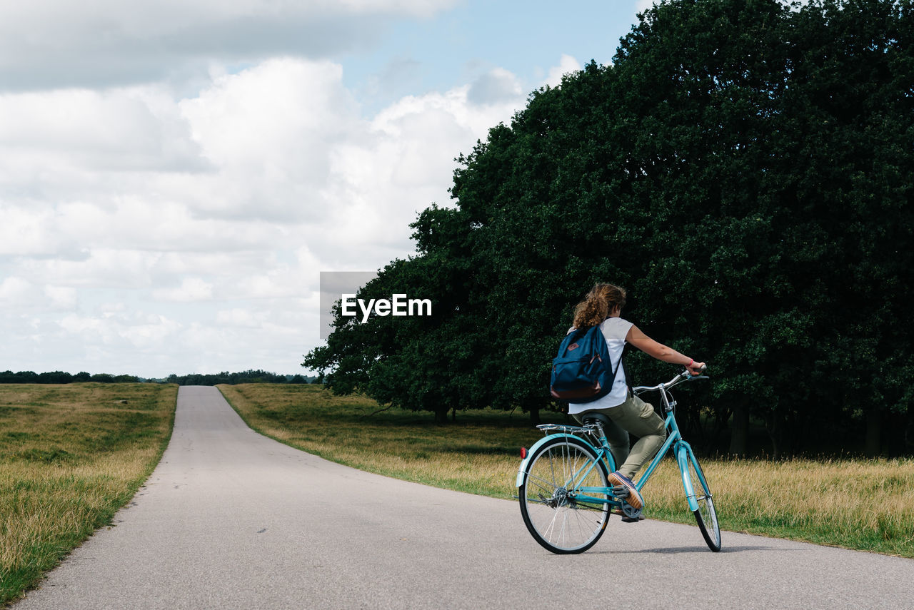 Woman riding bicycle on road against sky