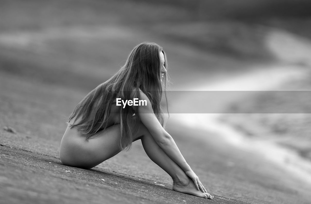 Naked woman sitting at beach