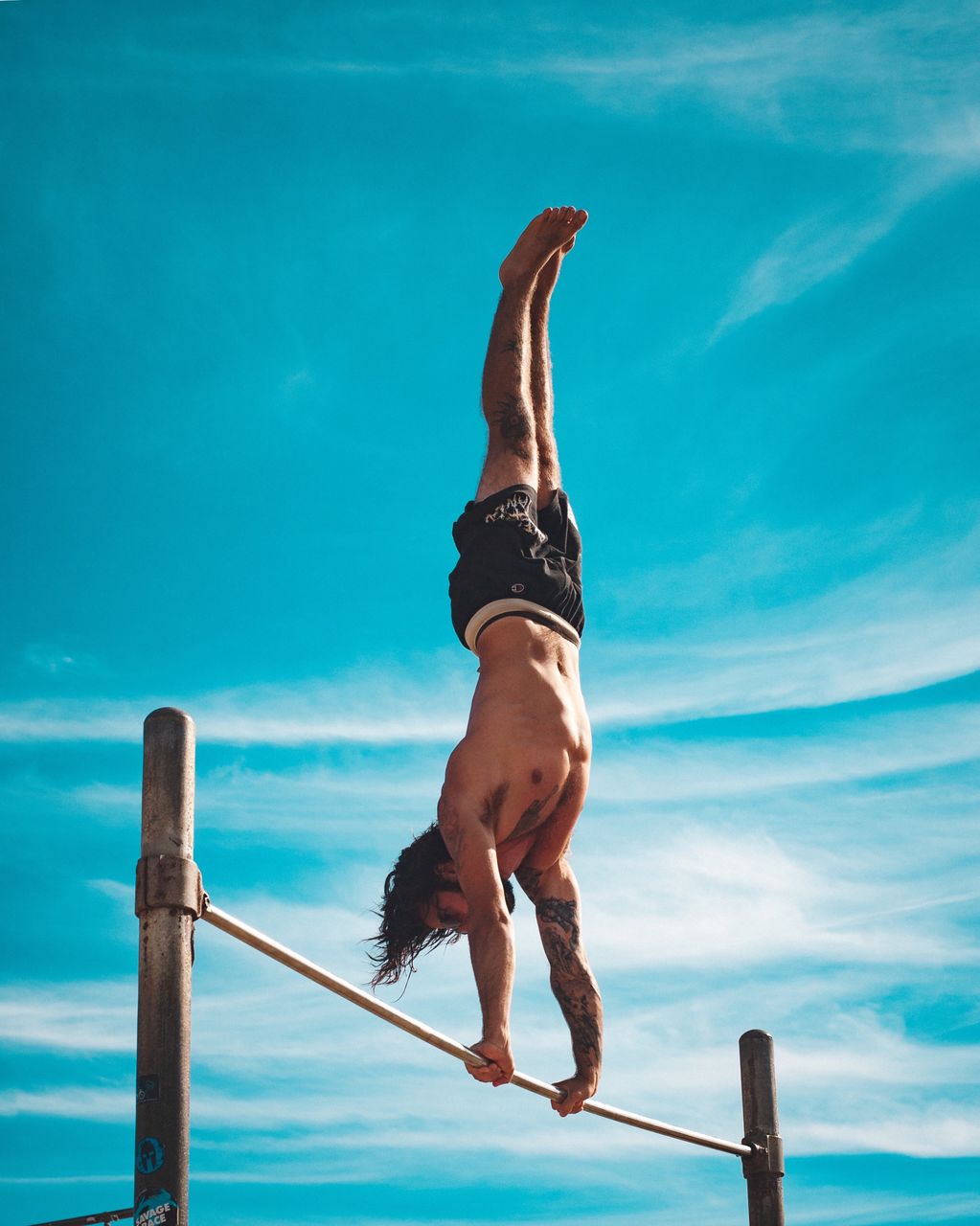Full length of shirtless man balancing on rope against blue sky