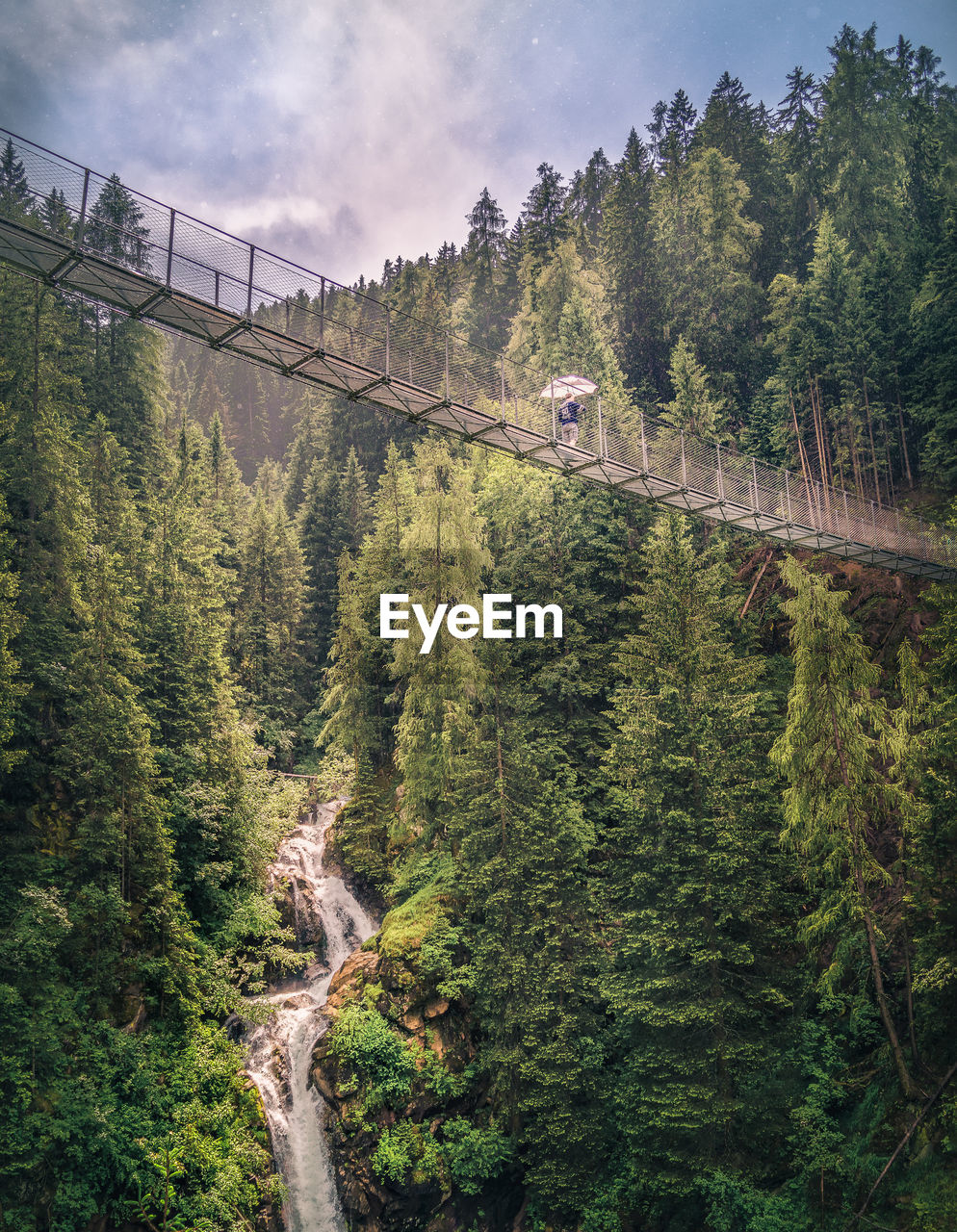 Person trekking footbridge in mountain scenery