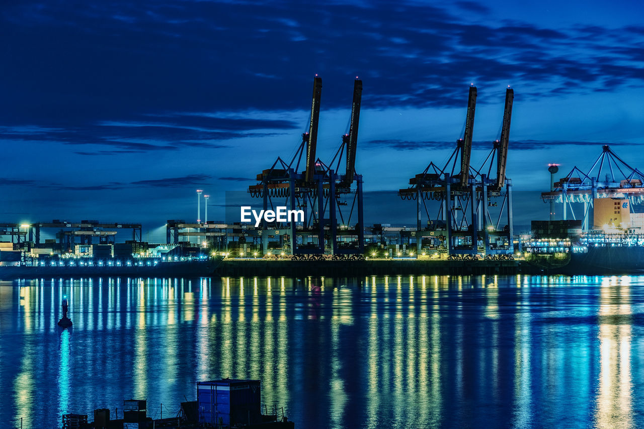 Illuminated city at harbor against sky during night