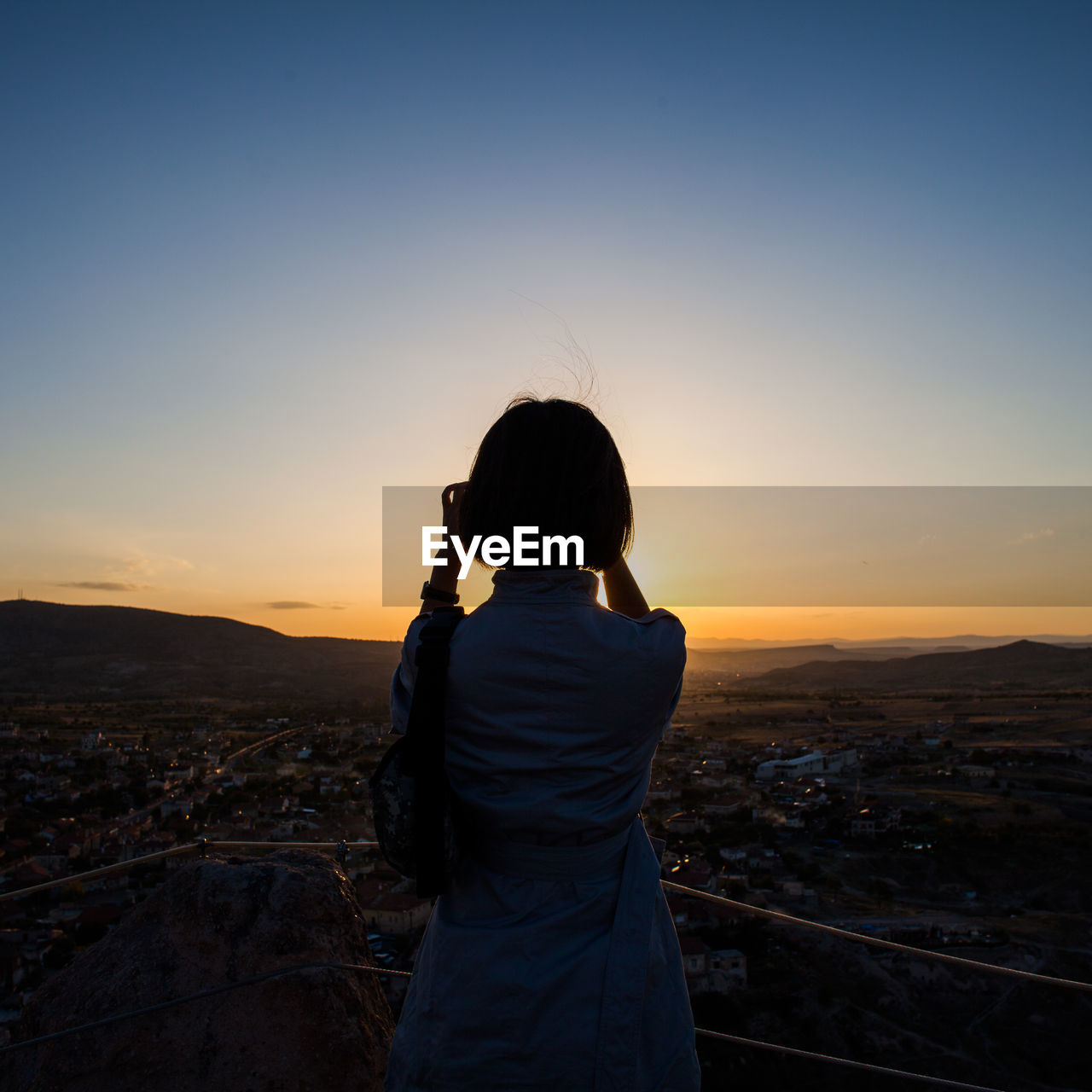 Rear view of woman standing at observation point against clear sky at sunset