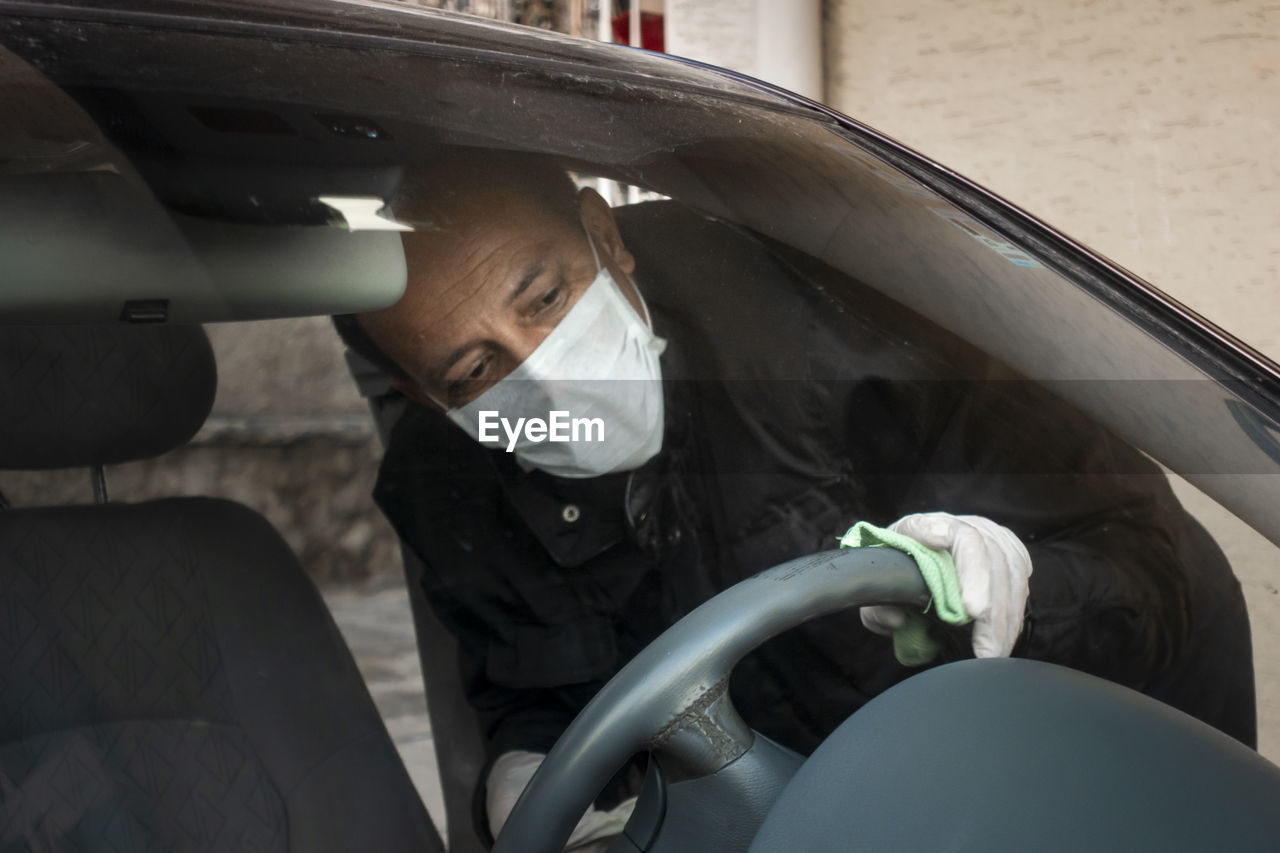 Man wearing mask cleaning steering wheel in car