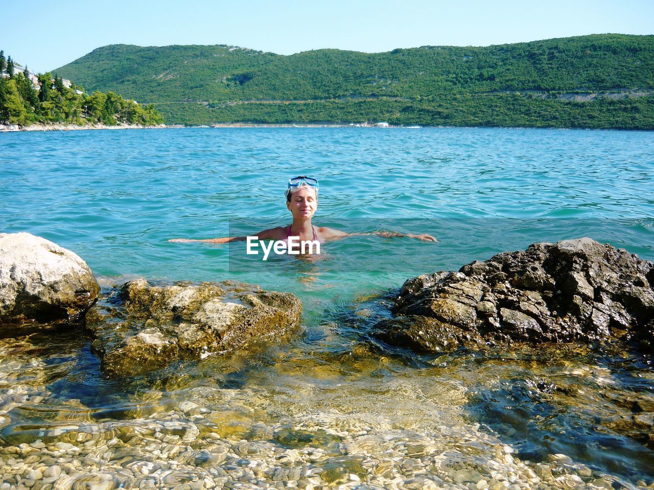 Scenic view of woman in sea surrounded by tree covered hills