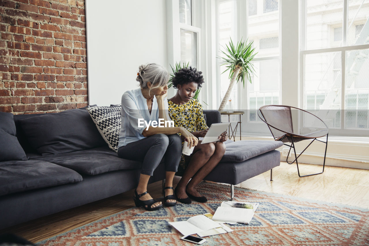 Businesswomen using tablet computer on sofa in creative office