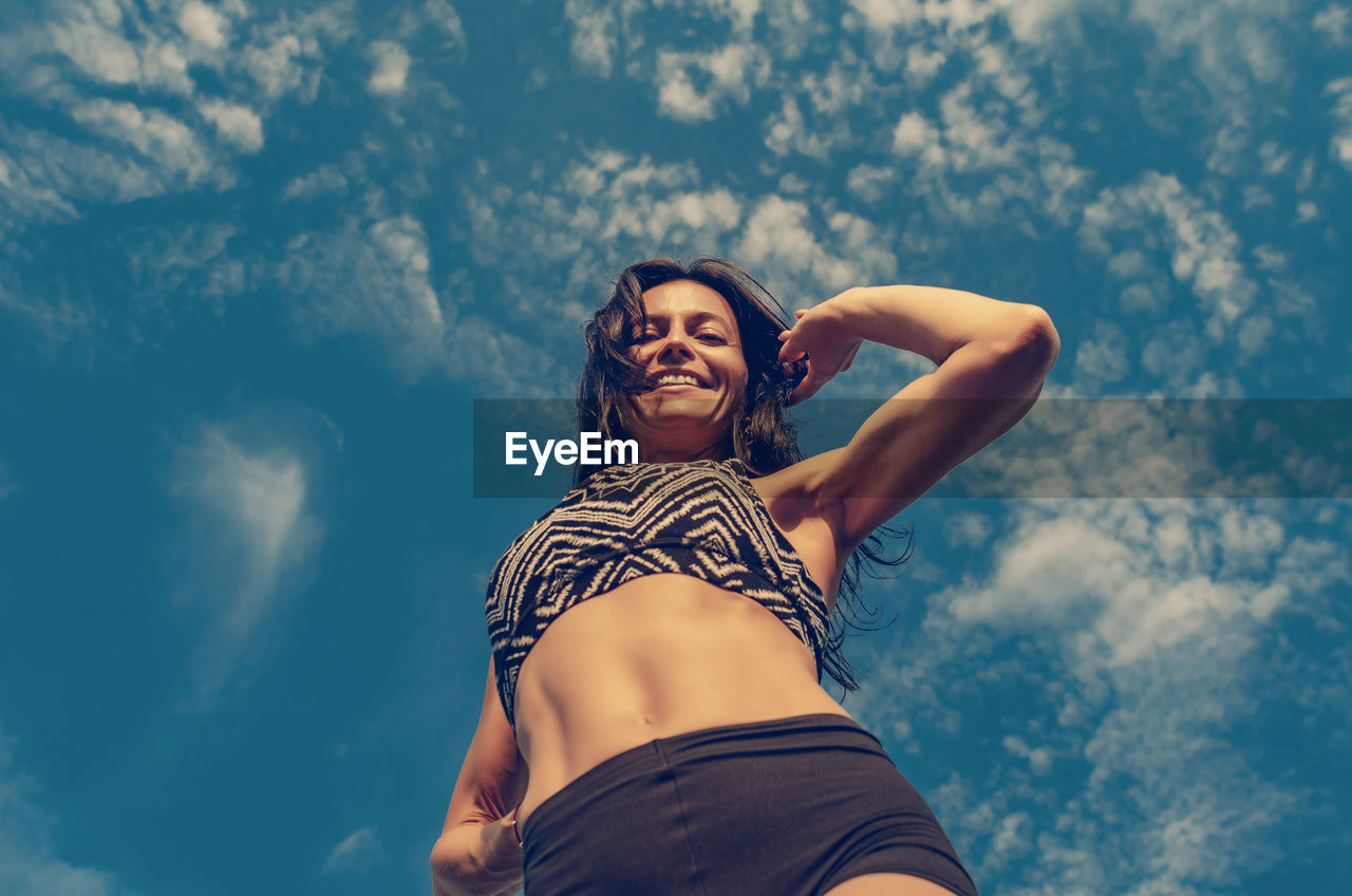 Woman athletic physique, sports shorts, top. bottom view on blue sky background.
