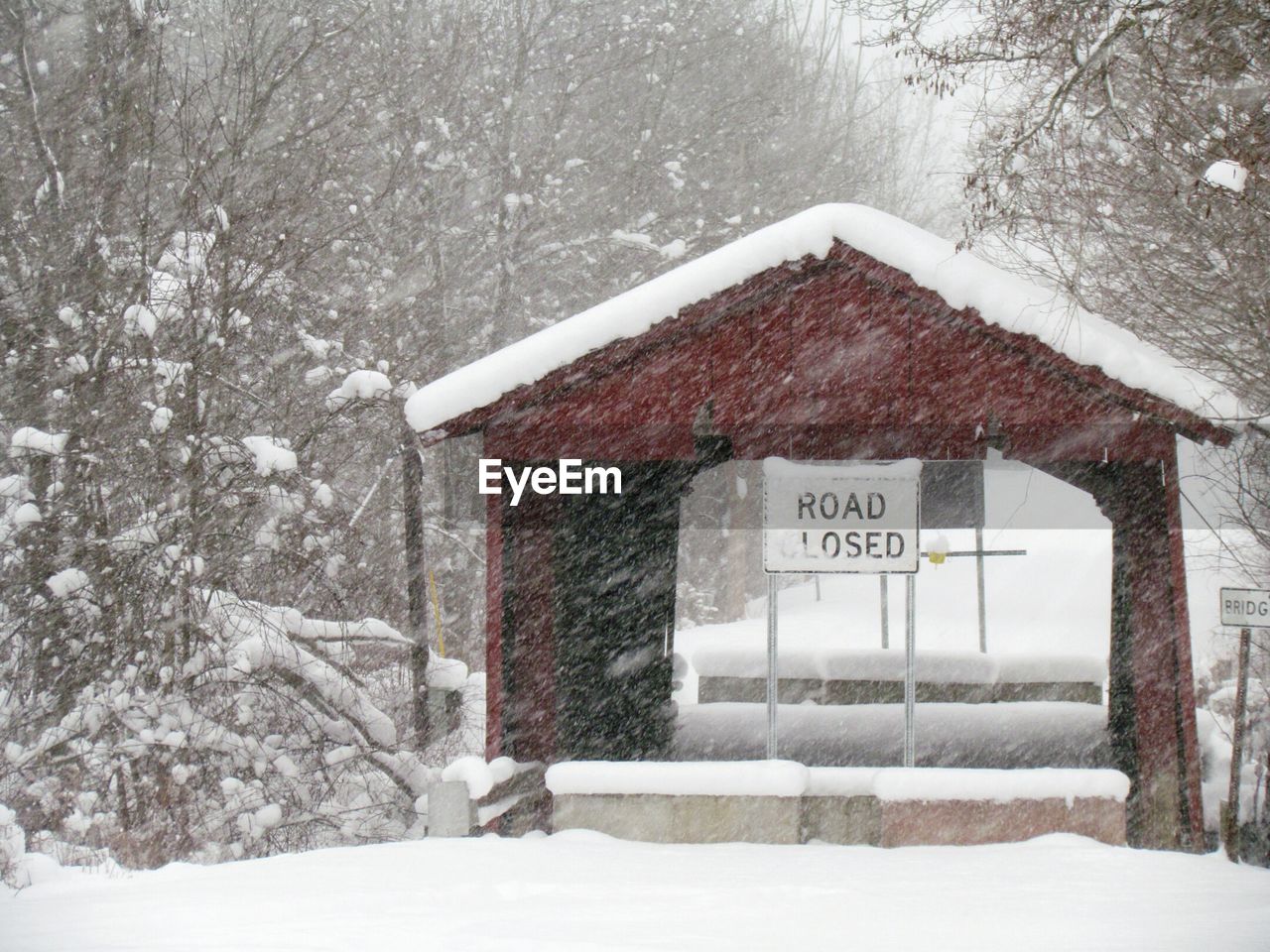Road closed sign on built structure in snowy weather