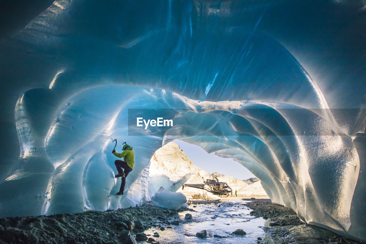 Man ice climbs inside glacial cave during helicopter adventure tour.