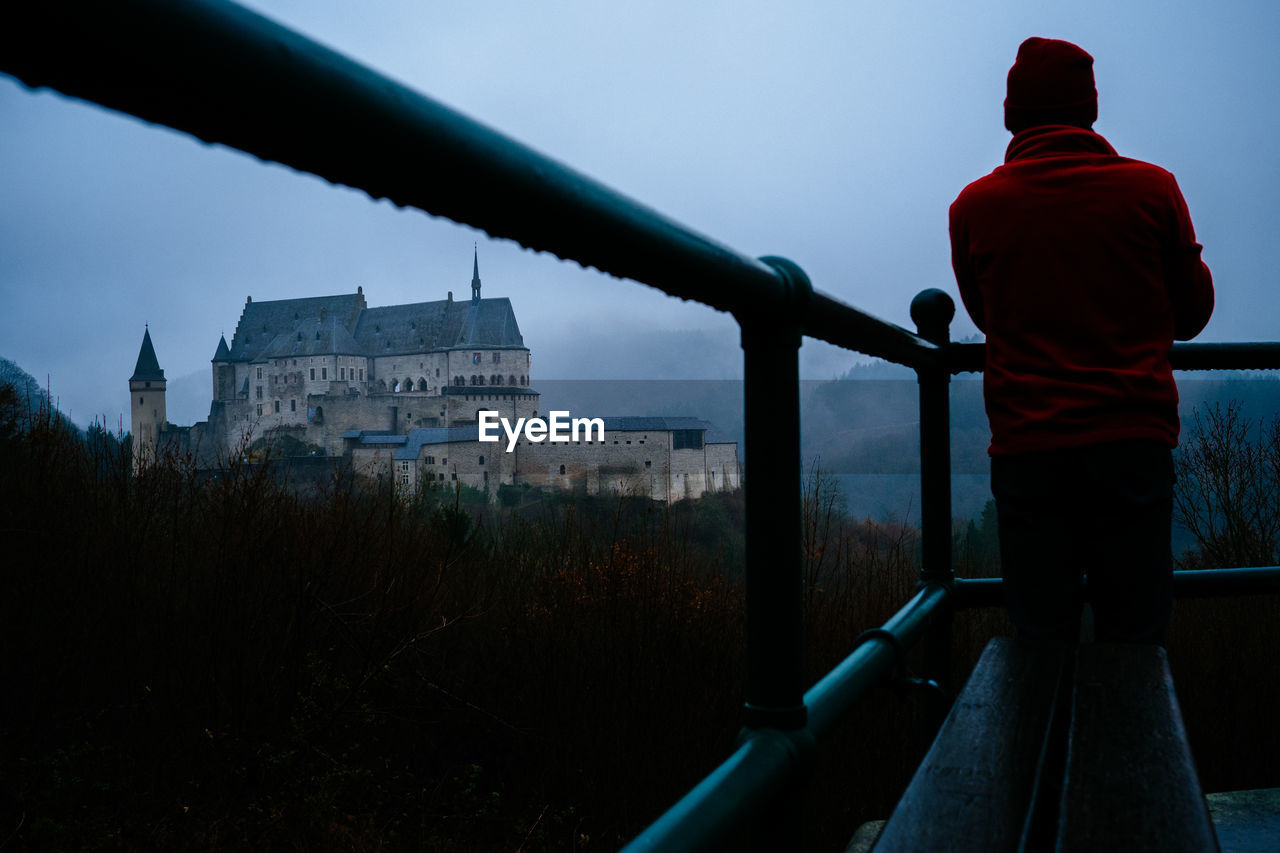Rear view of man standing by railing against vianden castle