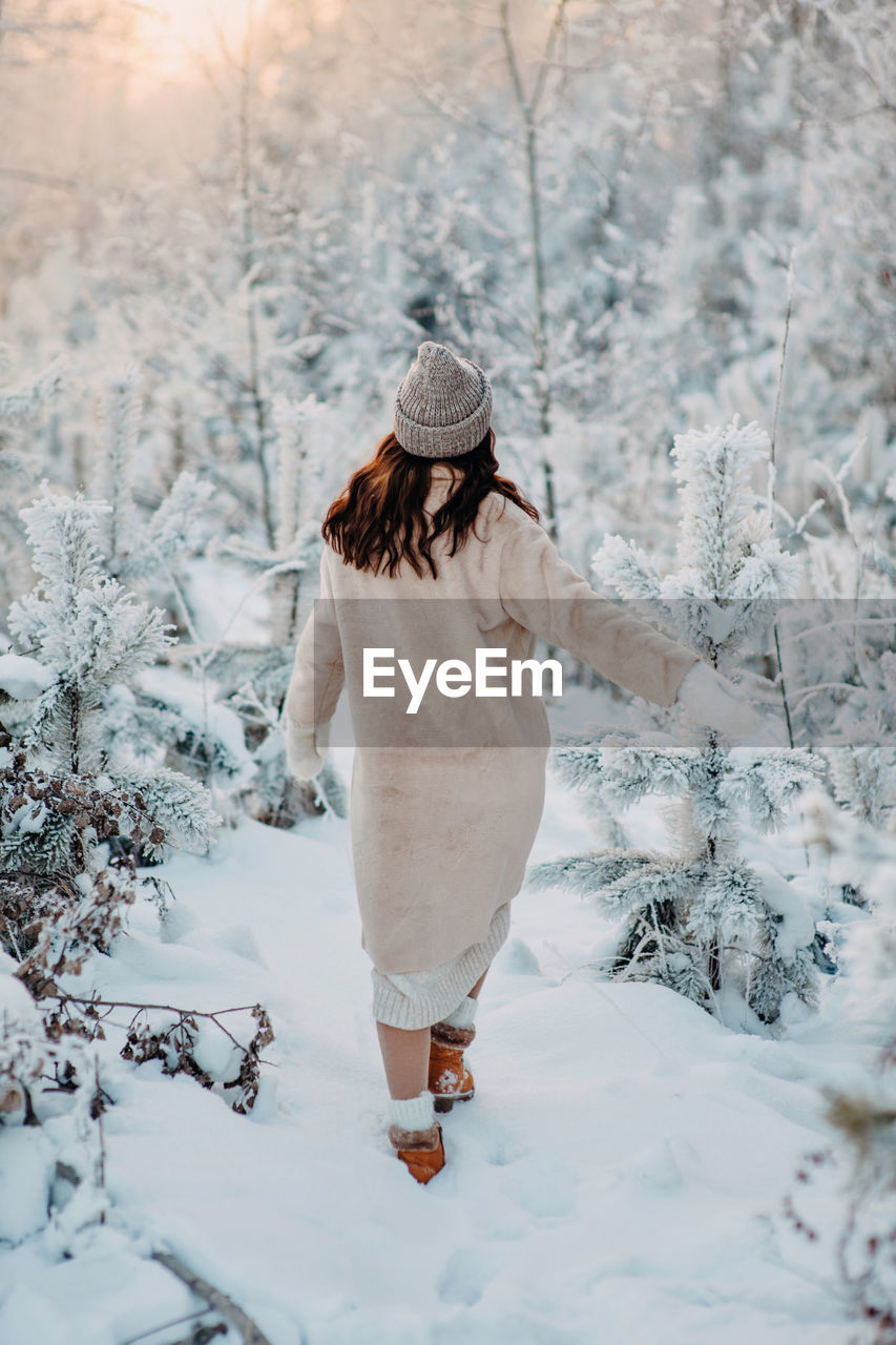 A girl in a beige faux fur coat walks through a snowy forest. fashionable winter look. stylish 