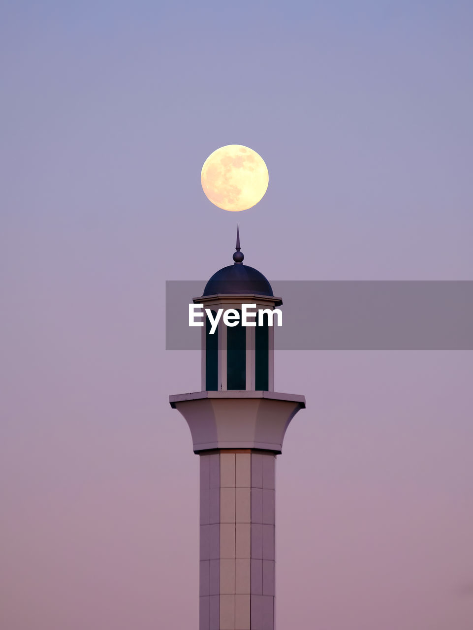View of a full moon rising above a tower against sky during sunset