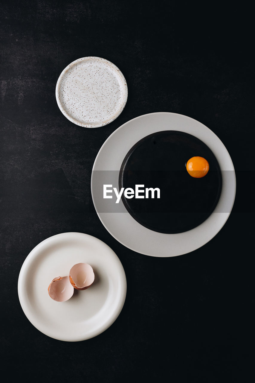 Creative concept idea of rounded black and white plates with egg yolk and shell. 
