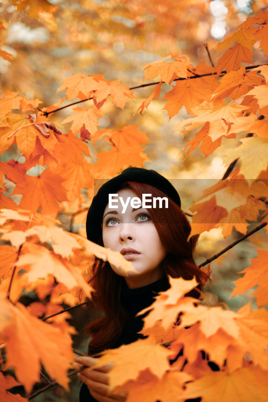 PORTRAIT OF YOUNG WOMAN WITH AUTUMN LEAVES IN TREE