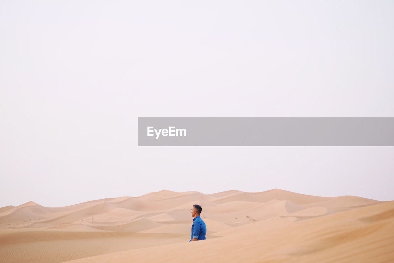 Side view of man amidst sand dunes at desert against clear sky