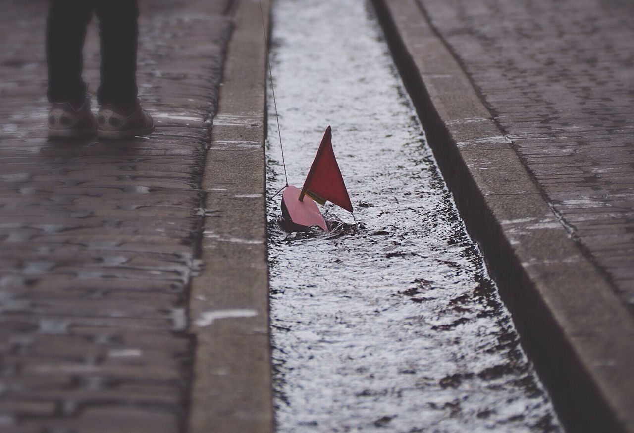 Toy boat in canal amidst sidewalk