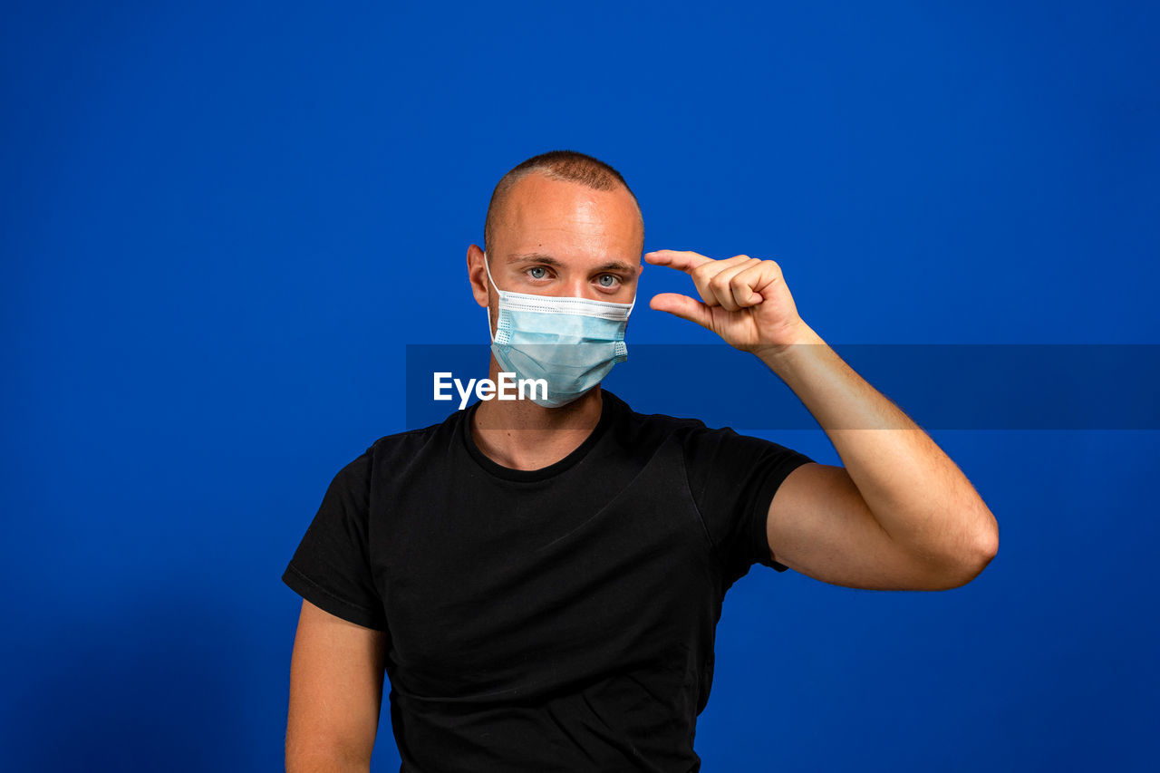 blue, one person, studio shot, adult, men, colored background, healthcare and medicine, portrait, blue background, arm, indoors, person, front view, waist up, clothing, looking at camera, copy space, human face, standing, finger, medical, illness, young adult, protective mask - workwear, shaved head, medicine