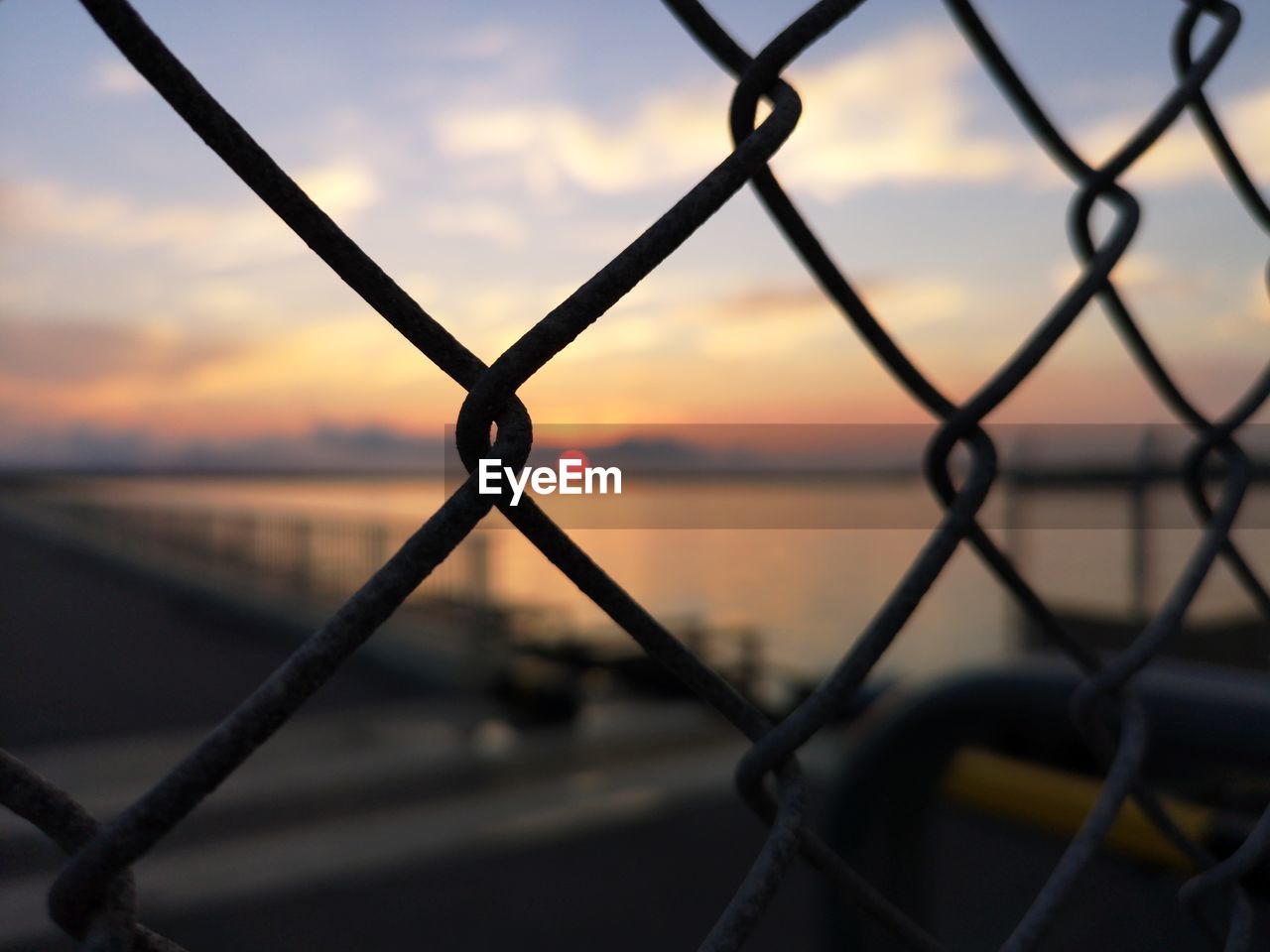 CLOSE-UP OF CHAINLINK FENCE AGAINST SUNSET SKY