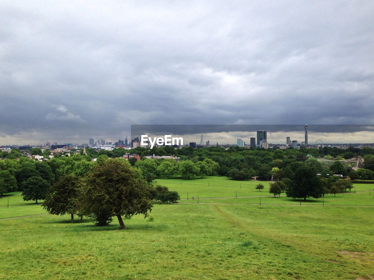 View of green landscape and cityscape against cloudy sky
