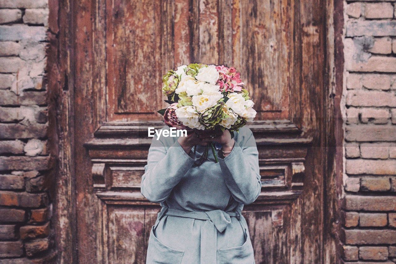 Woman with face covered by flowers against wooden door
