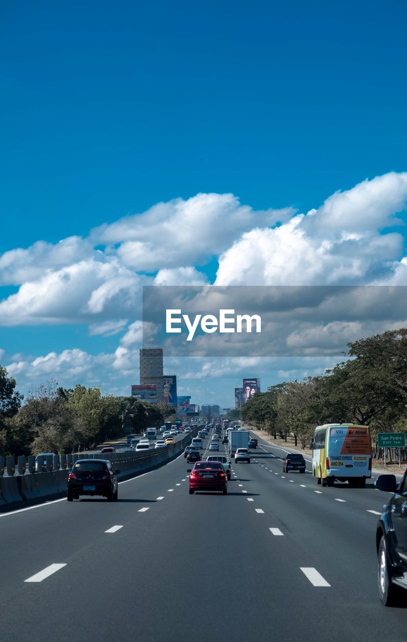 CARS ON ROAD AGAINST CLOUDY SKY
