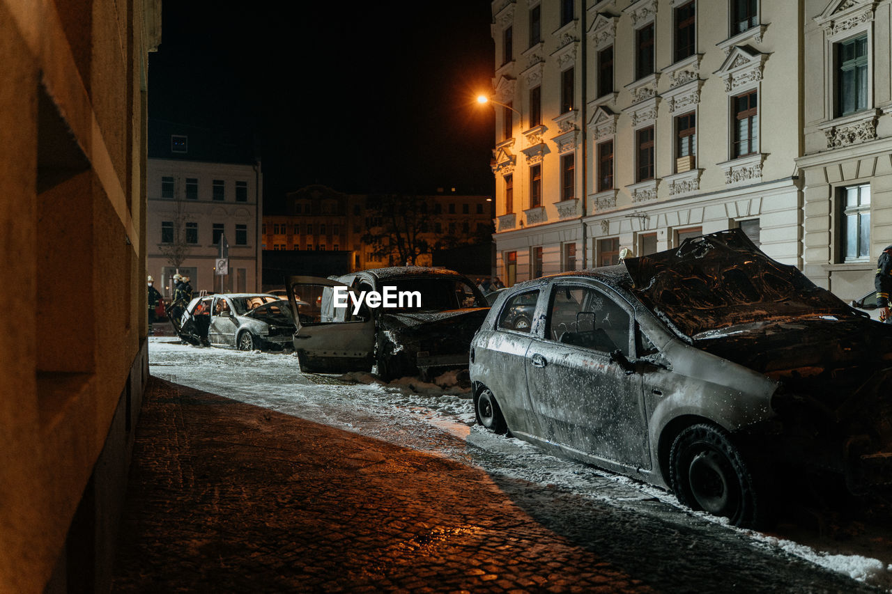 Abandoned cars parked on street by buildings in city at night