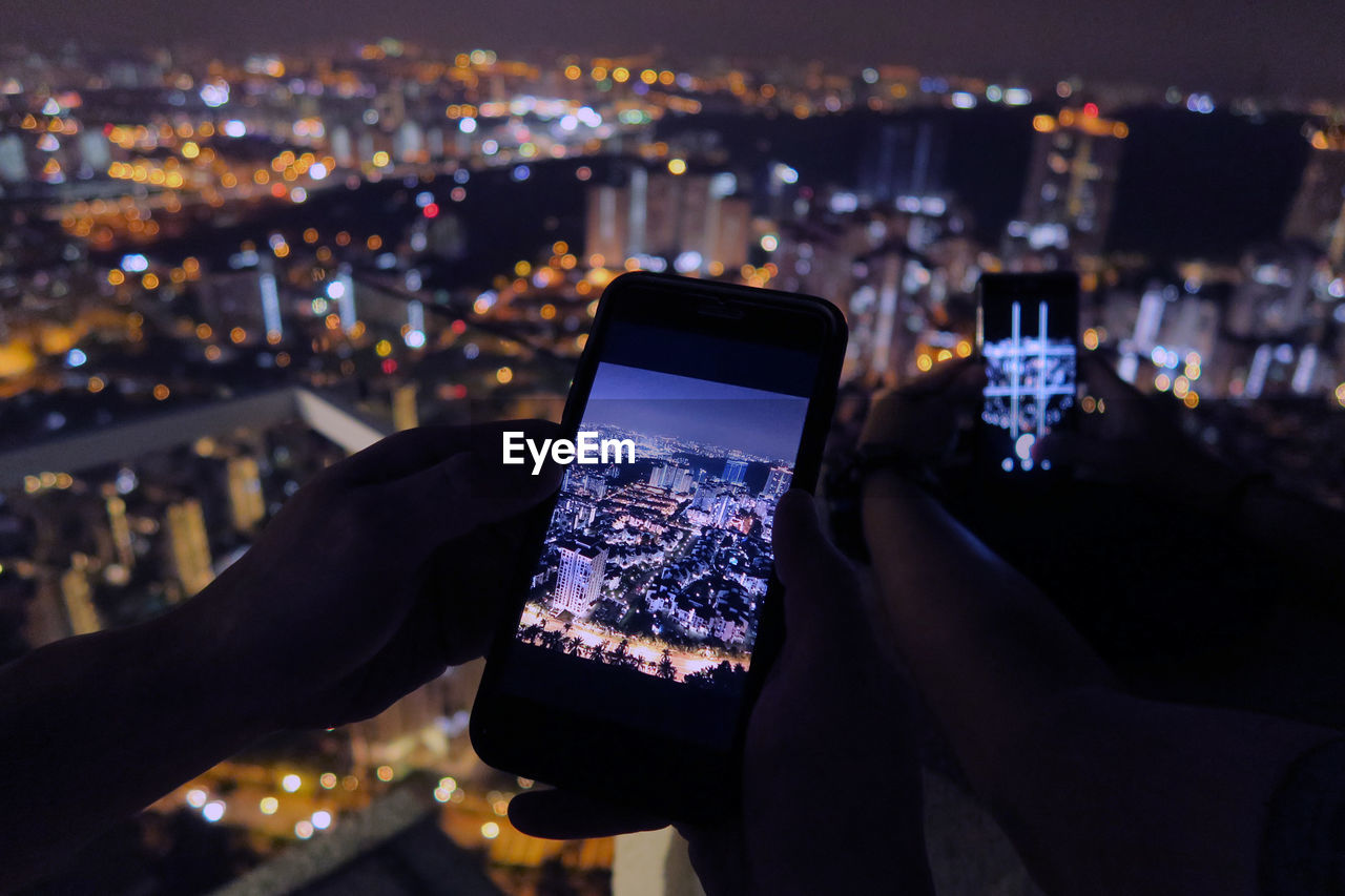 Cropped image of friends photographing illuminated cityscape through smart phone