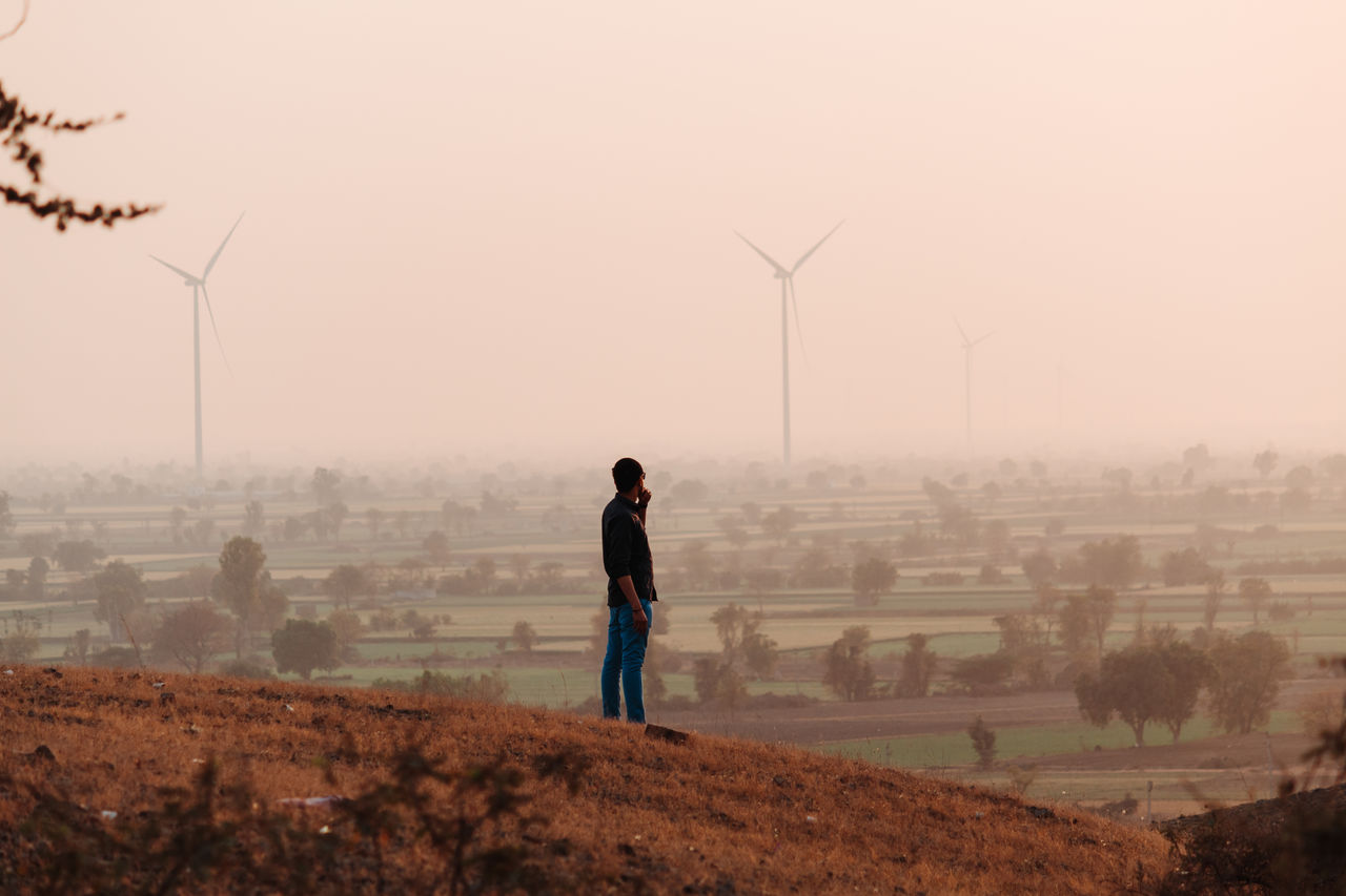 Man standing on hills against windmills