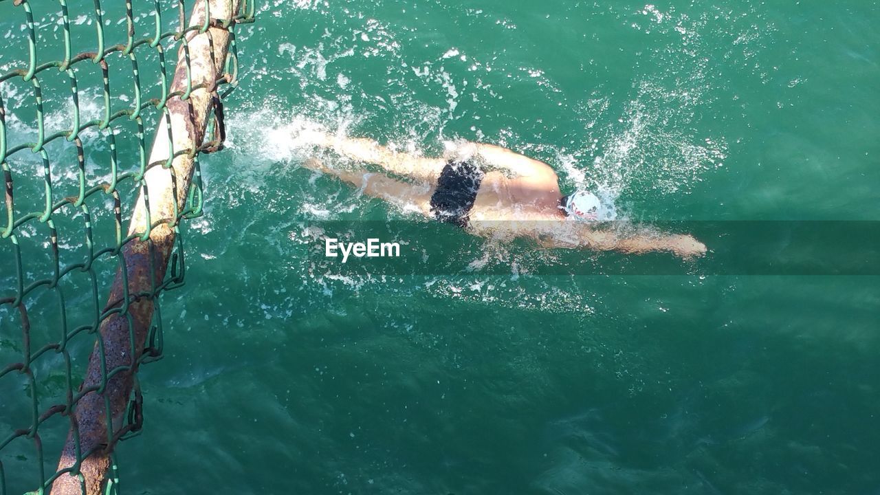 High angle view of swimmer swimming in pool below fence