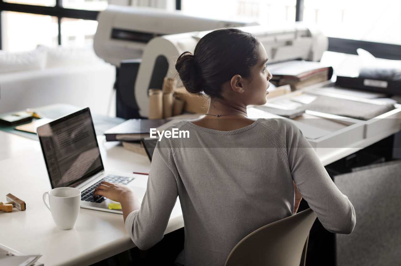 Rear view of interior designer looking away while working at desk in office