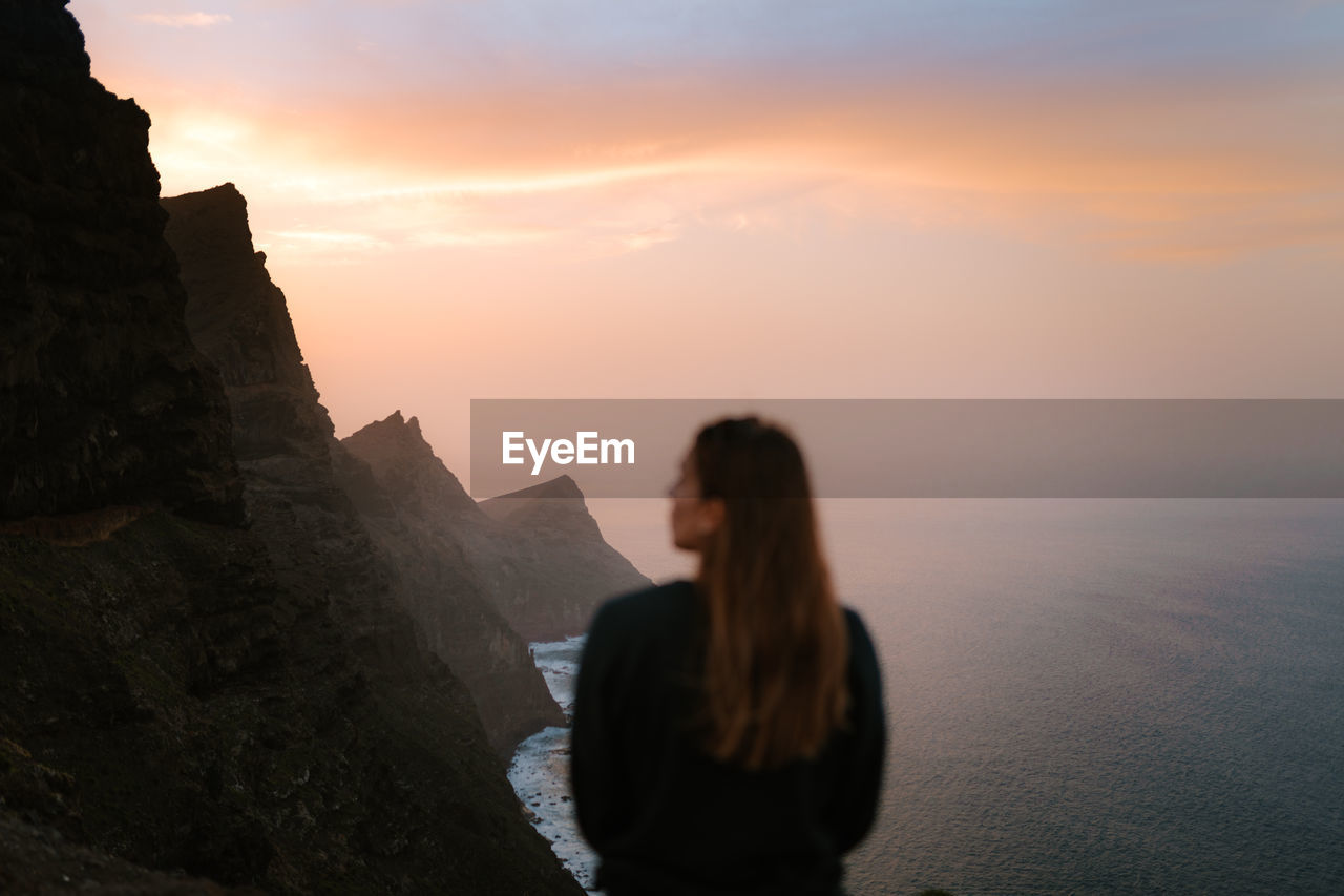 Girl out of focus looking away in front of big cliffs