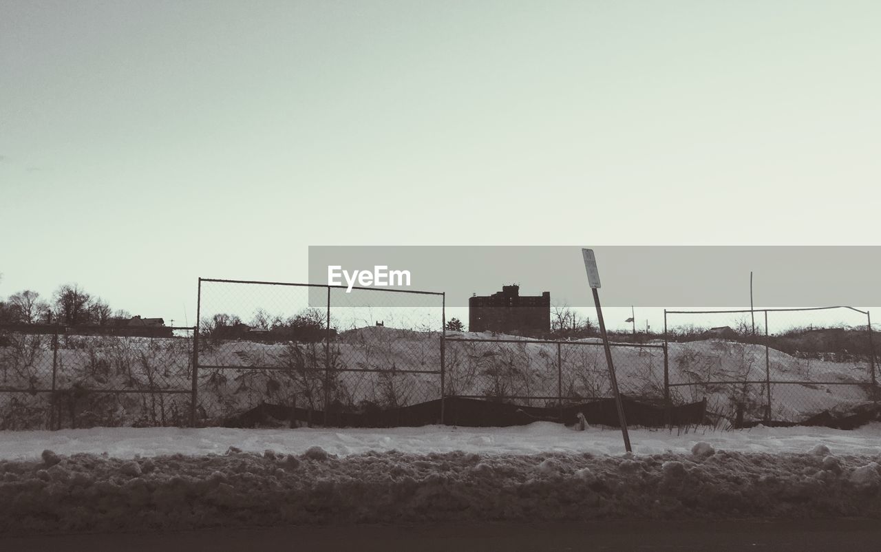 Fence at snow covered field against clear sky