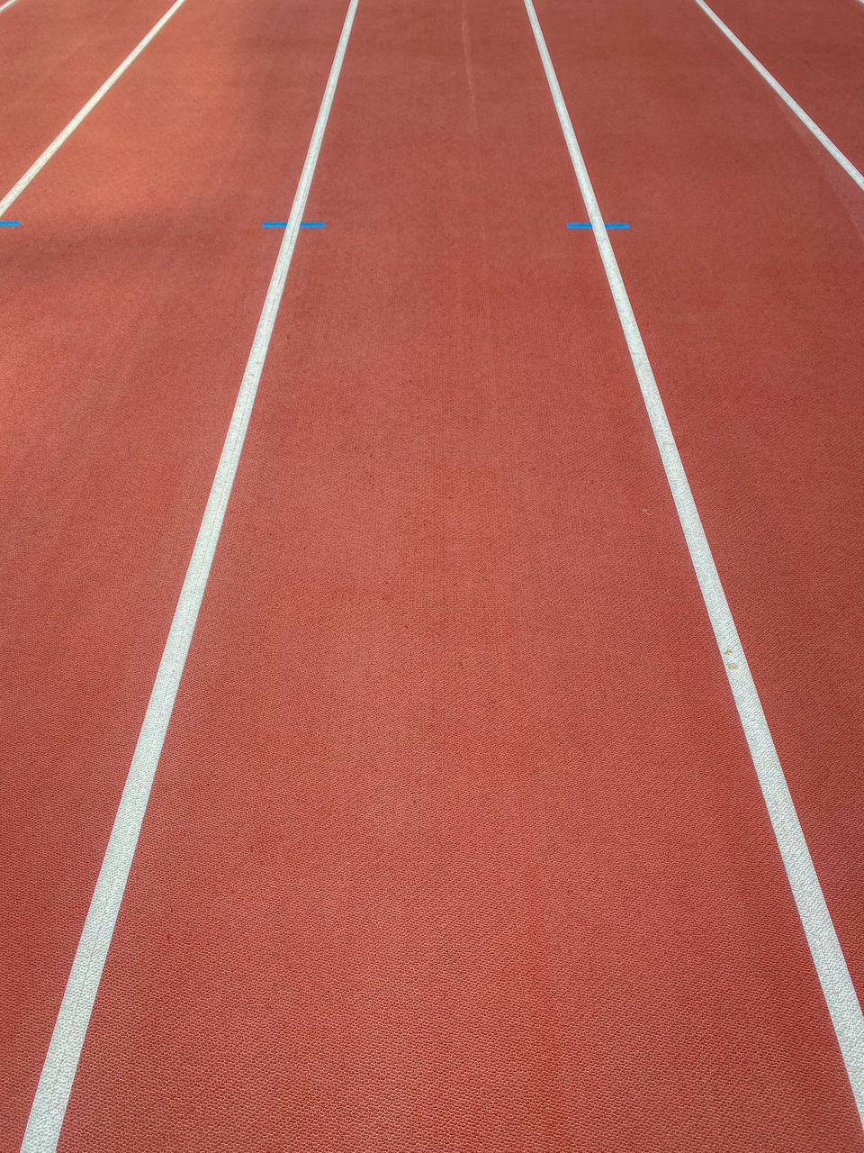 Lane on a red athletics track with white lines and blue marks