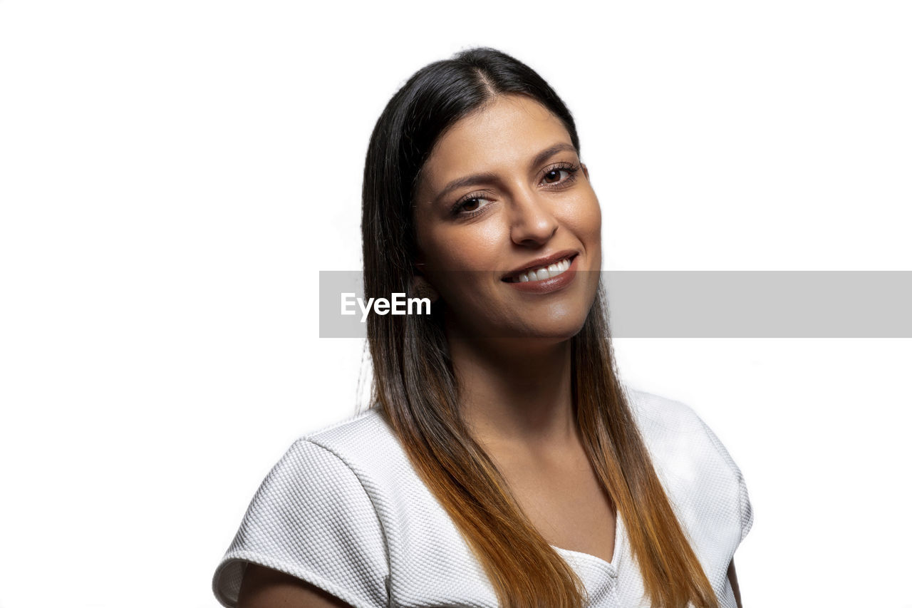 PORTRAIT OF A SMILING YOUNG WOMAN AGAINST WHITE BACKGROUND