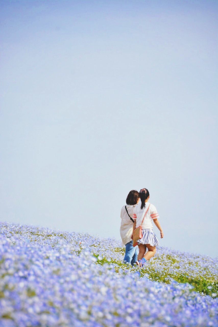 Rear view of mother and daughter walking on purple flowerbed