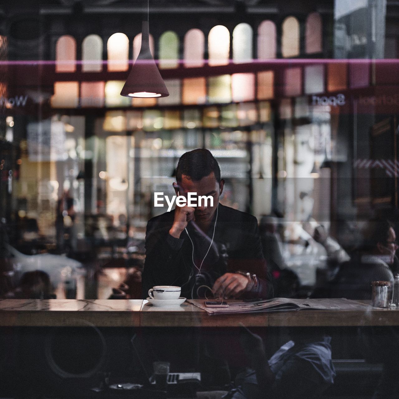 Man using phone on table in cafe seen through window