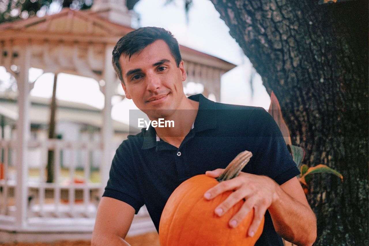 Portrait of young man smiling while holding pumpkin outdoors