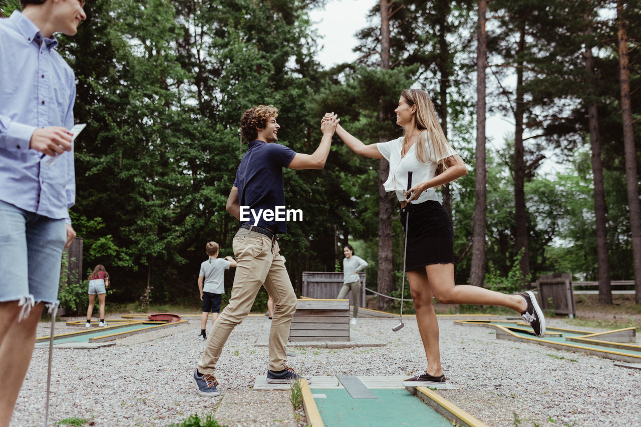 Full length of friends giving high-five while playing miniature golf in backyard