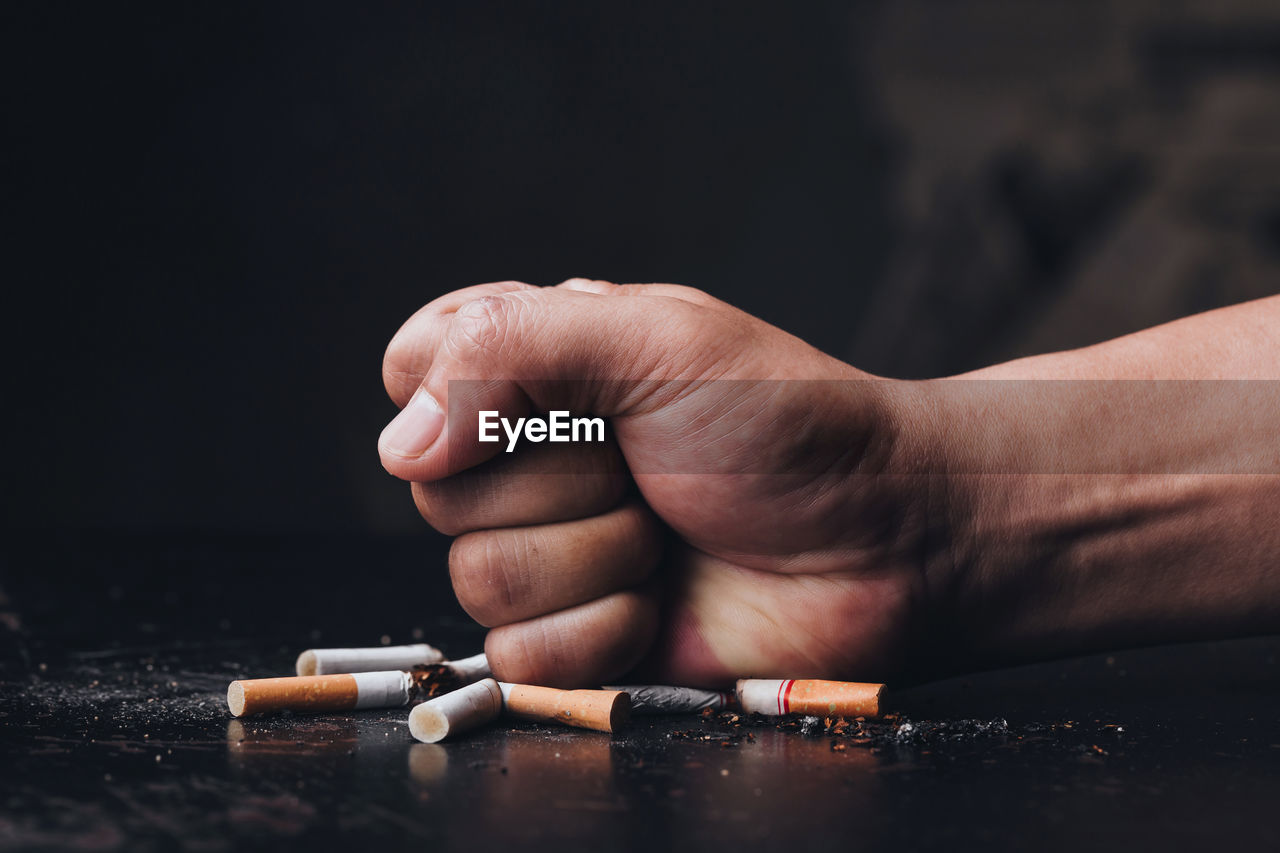 Cropped hand of person crushing cigarette against black background