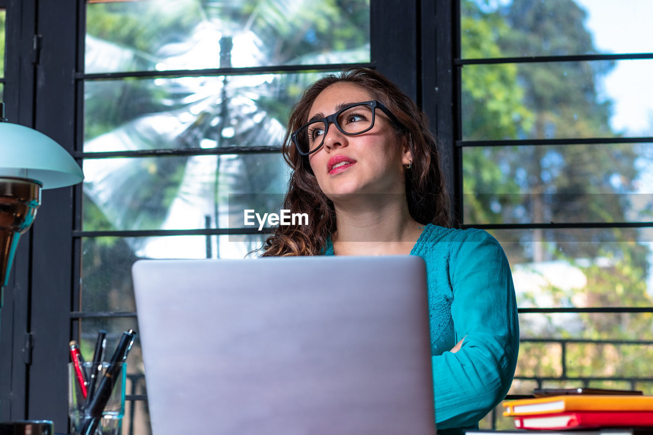 PORTRAIT OF YOUNG WOMAN USING MOBILE PHONE IN BUILDING