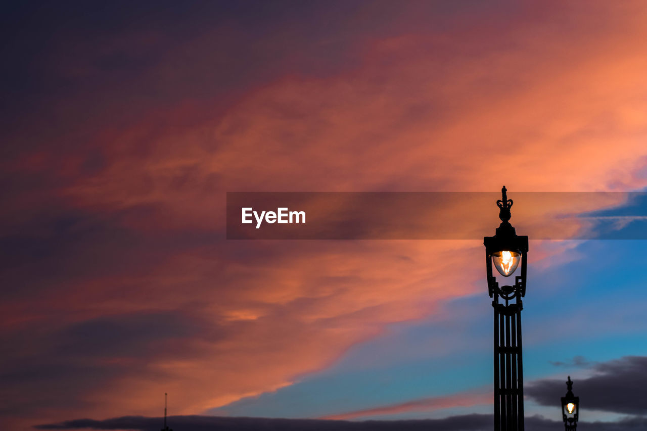 Low angle view of illuminated lamp post against orange sky