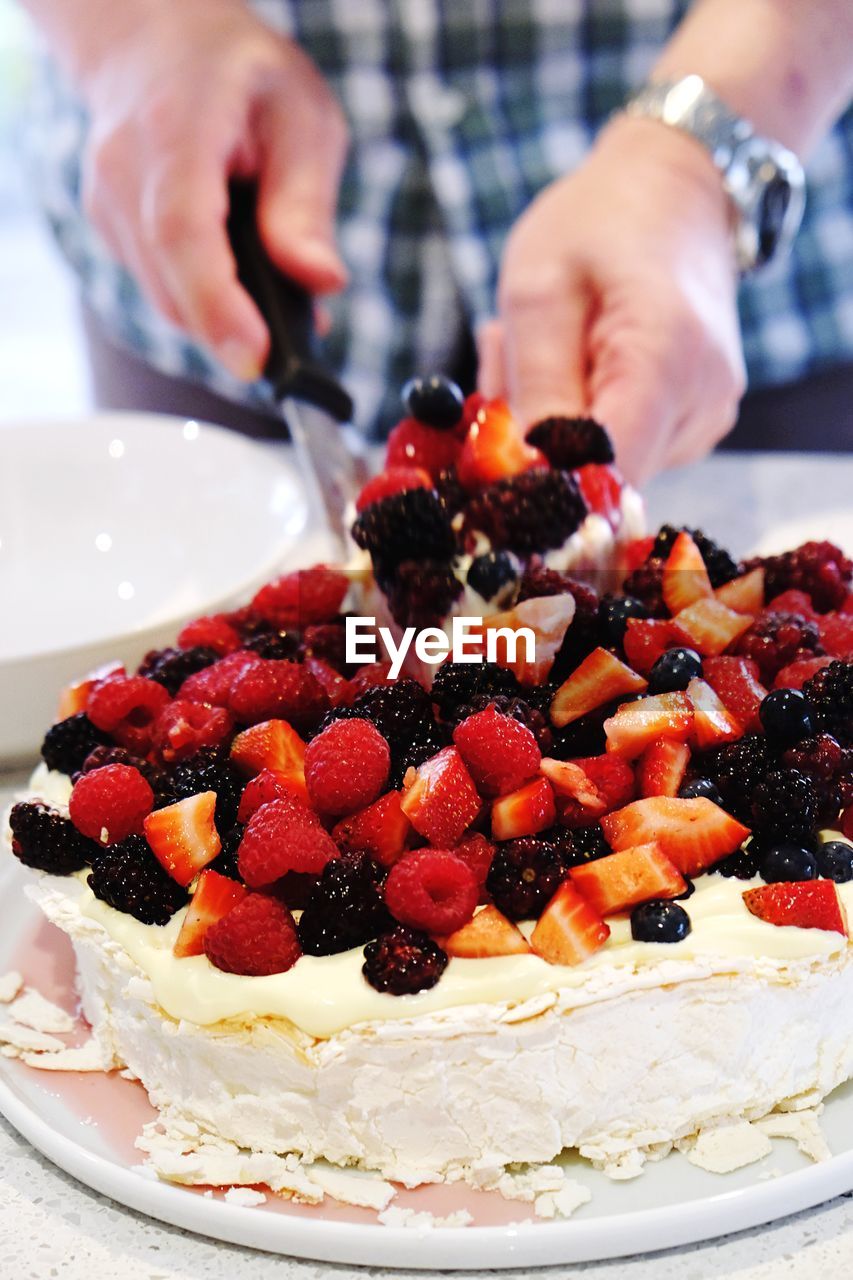 Midsection of man cutting pavlova on table