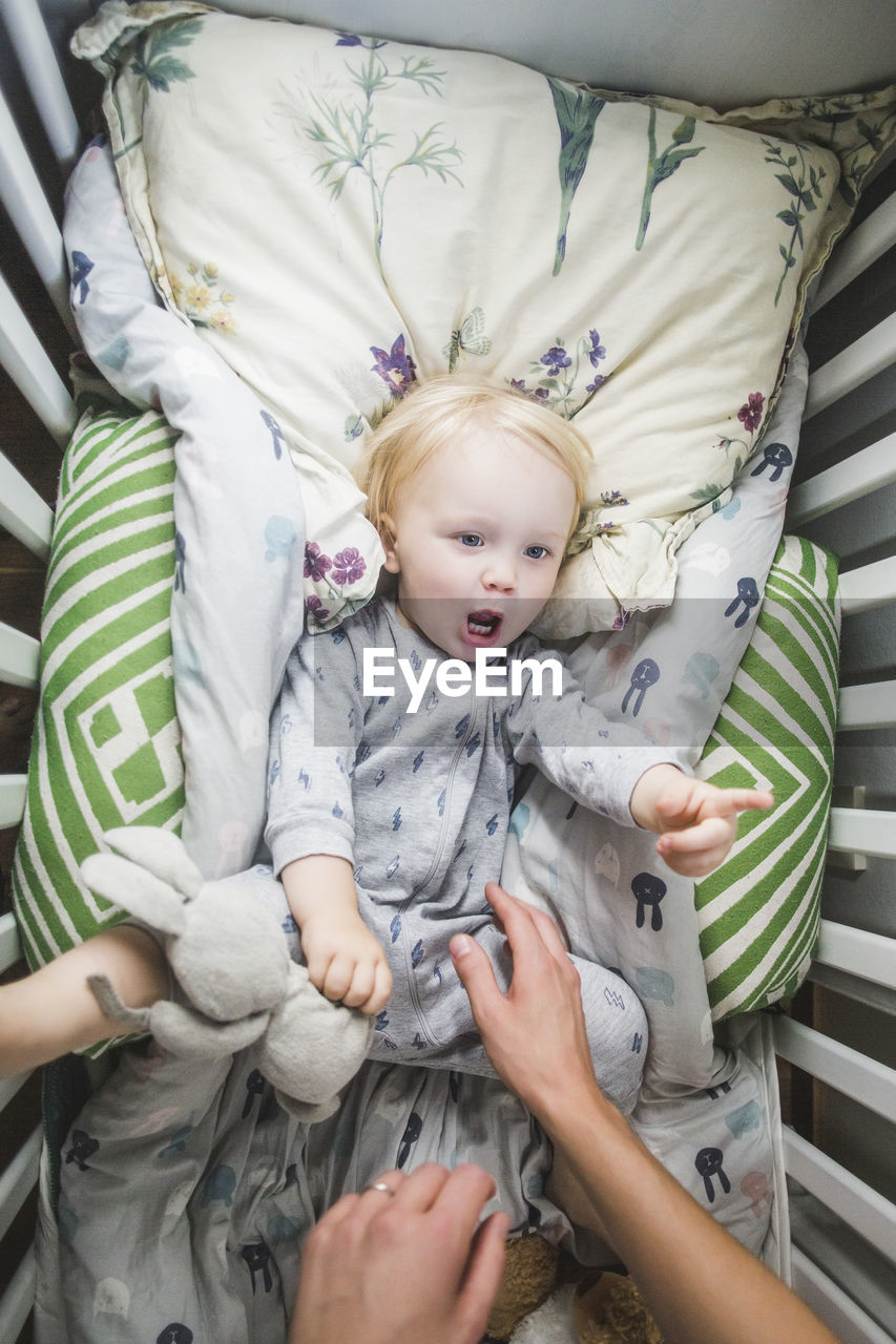 Directly above view of baby boy lying in crib while pointing and looking at father
