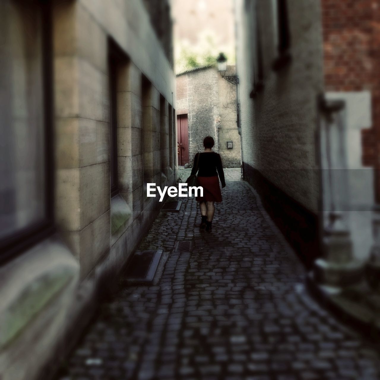 Rear view of woman walking on narrow cobblestone street